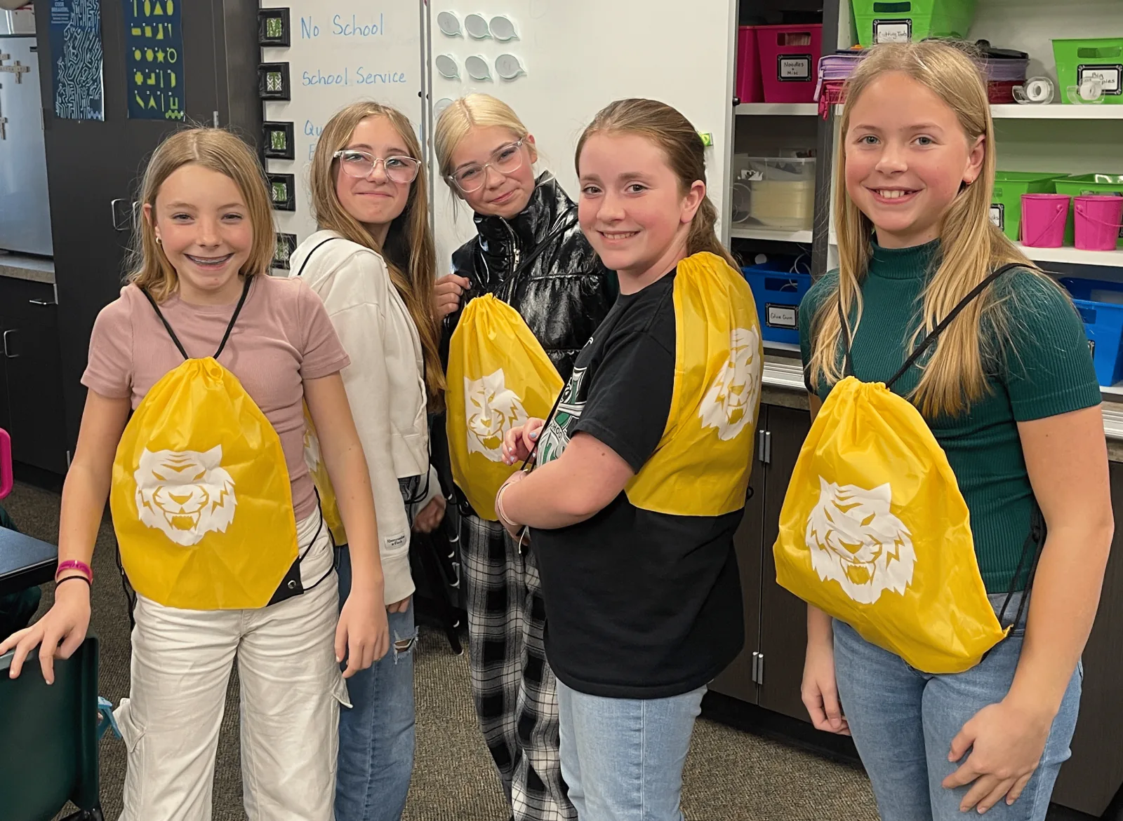 Five girls smile together wearing matching yellow tiger-mascot drawstring bags